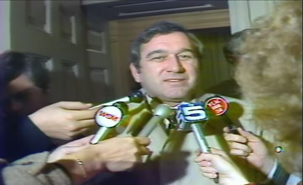 photo of man surrounded by reporters' microphones