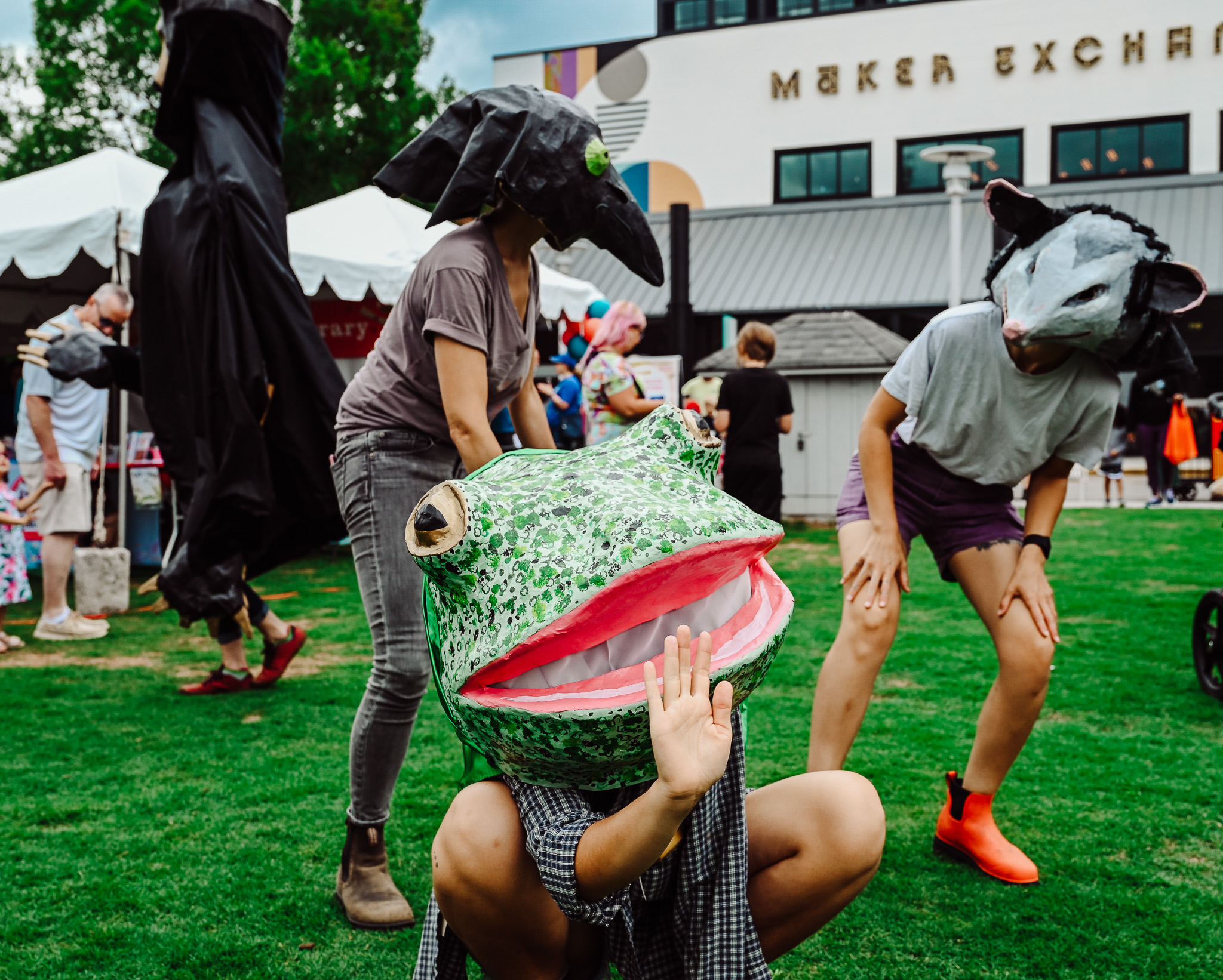 photo of individuals wearing large painted Papier-mâché animal heads- frog, possum, and bird